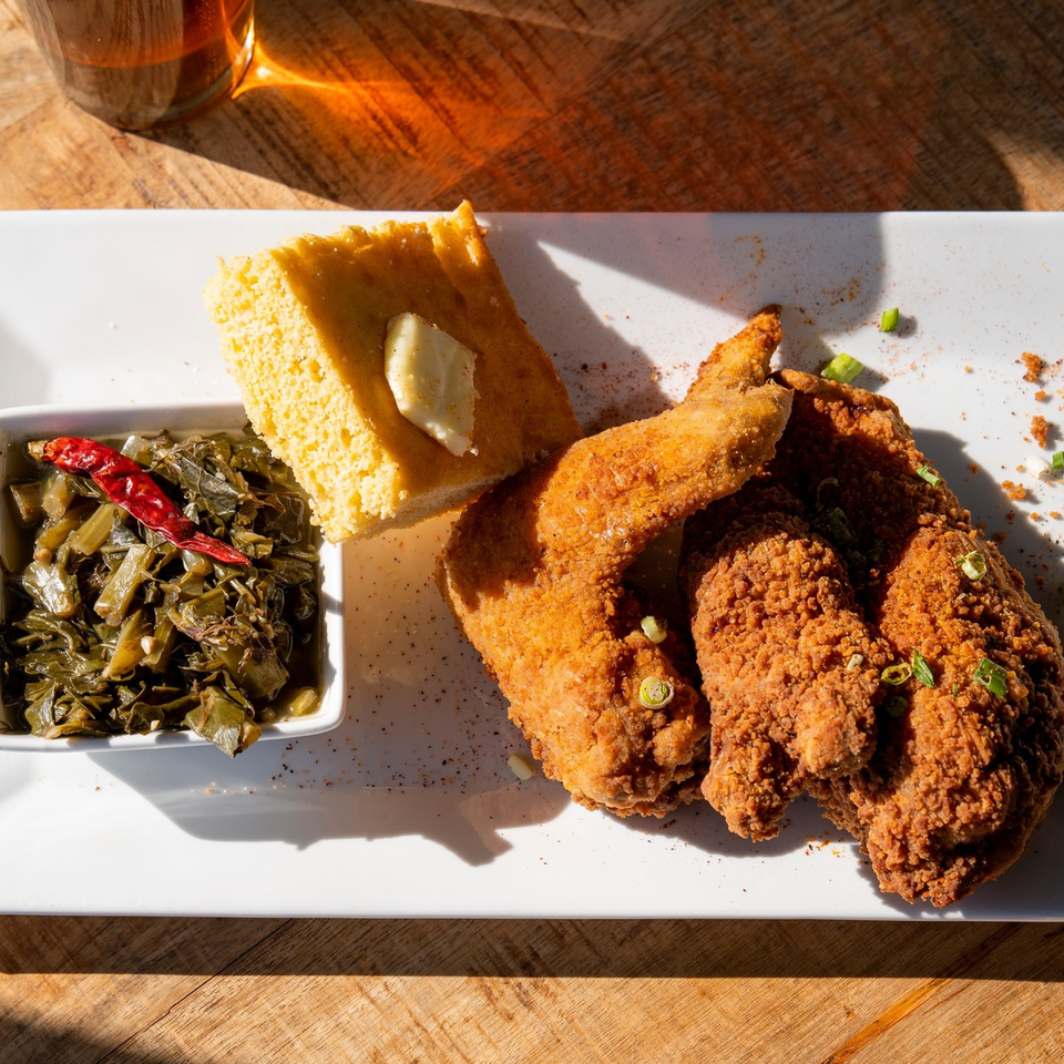 Crispy fried chicken, cornbread with butter, and collard greens with a red chili on a white plate.