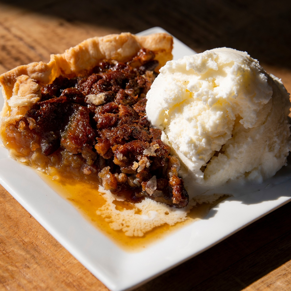 A slice of pecan pie with a scoop of vanilla ice cream on a white plate.